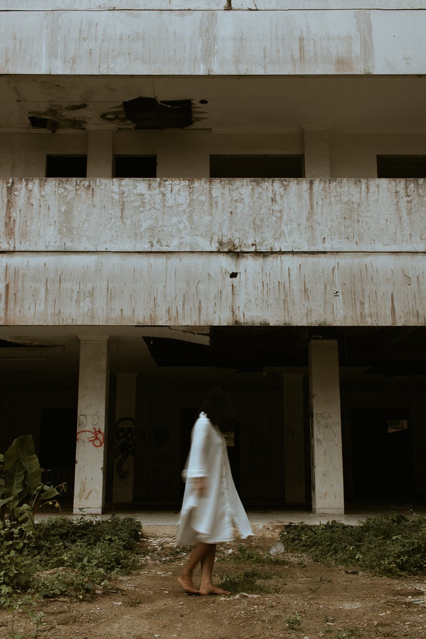 unrecognizable woman in white dress near abandoned building